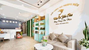 A modern hotel lobby with a reception desk, a sofa, a coffee table, and a wall with a sign. - THE COZY INN (Ho Chi Minh City)