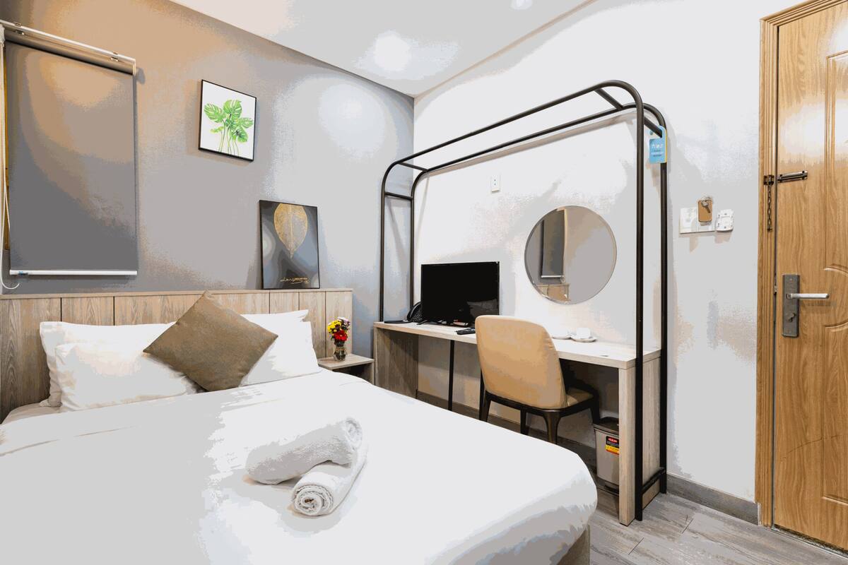 Een hotelkamer met een bed, een bureau met een computer, een stoel, een spiegel en een houten deur.
