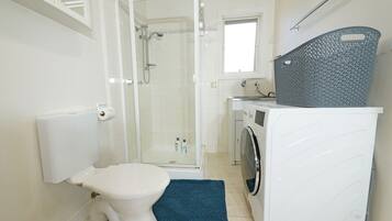 Ein Badezimmer mit Toilette, Dusche, Waschmaschine und Wäschekorb.