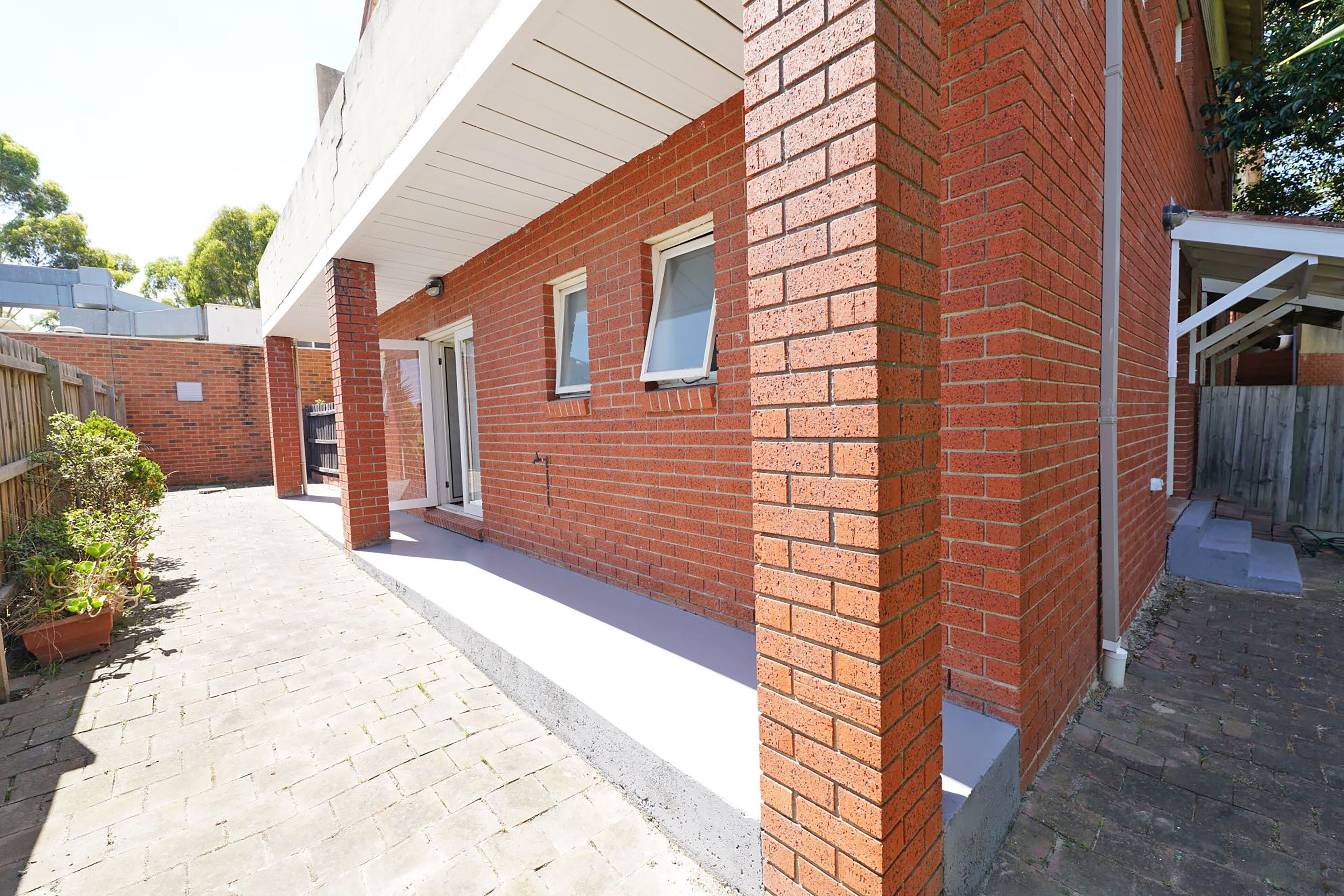 Un bâtiment en briques rouges doté d’un patio couvert, d’une porte et d’une petite fenêtre.
