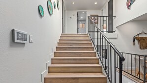 Una escalera de madera con barandillas negras que conduce a una plataforma con una puerta y un interruptor de luz en la pared.