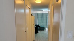 Un estrecho pasillo con paredes blancas y piso alfombrado que conduce a una habitación con cama y ventana.