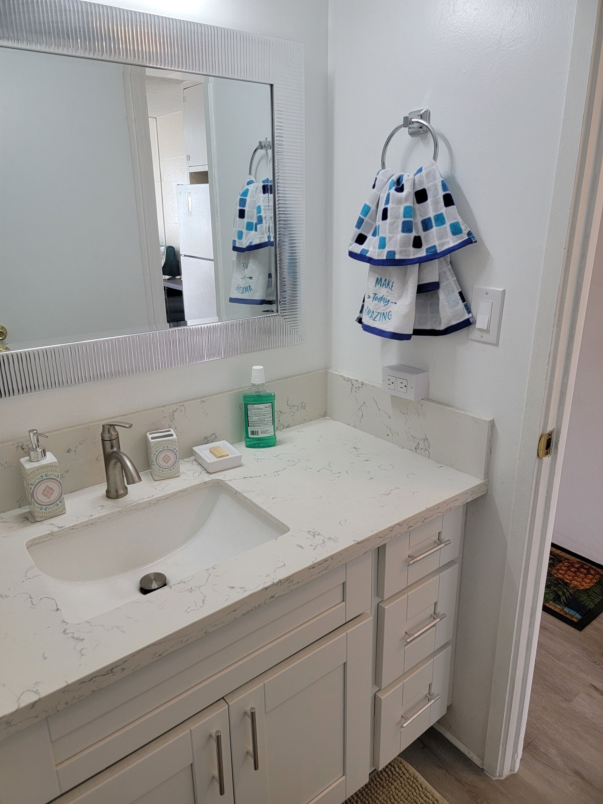 A bathroom with a white sink, a mirror, a towel rack with towels, a soap dispenser, and a toothbrush holder.