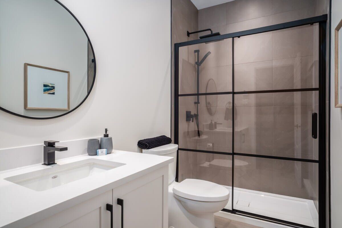 A modern bathroom with a large mirror, two sinks, a toilet, and a glass-enclosed shower.
