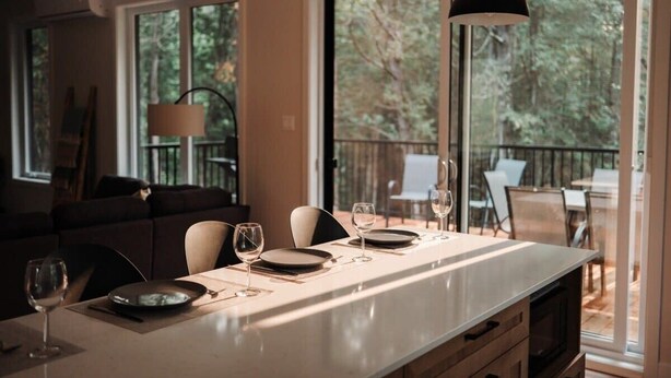 A modern kitchen with a central island, large windows, and a view of the outdoors. - Nature Escape Near Tremblant: Hot Tub & Lake access (Amherst)