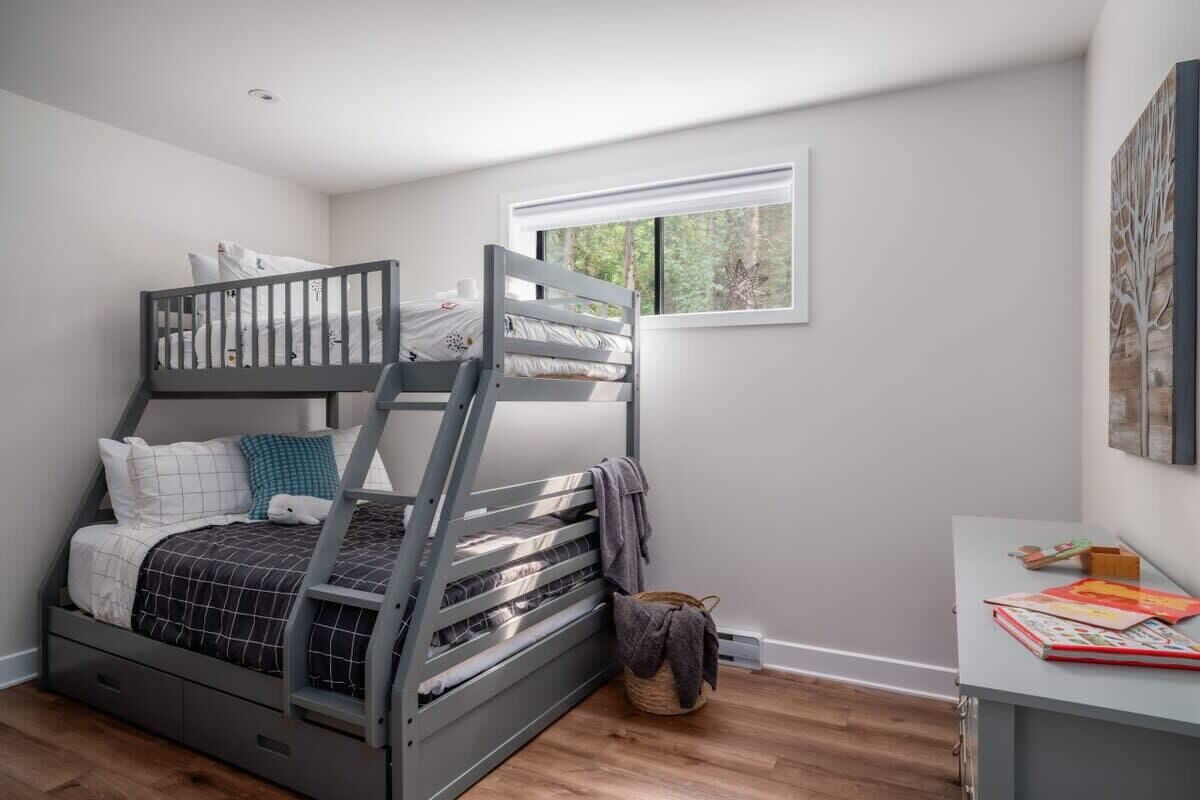 A bedroom with a bunk bed, a desk with books, and a window with a view of trees.