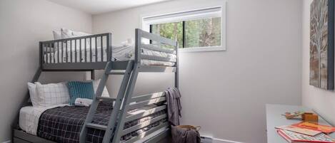 A bedroom with a bunk bed, a desk with books, and a window with a view of trees.