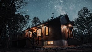 A wooden cabin with a balcony, a staircase, and a starry night sky. - Nature Escape Near Tremblant: Hot Tub & Lake access (Amherst)