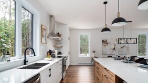 A modern kitchen with white cabinetry, a wooden countertop, and pendant lighting. - Nature Escape Near Tremblant: Hot Tub & Lake access (Amherst)