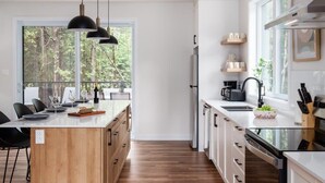 A modern kitchen with a wooden island, white cabinetry, and a large window offering a view of the forest. - Nature Escape Near Tremblant: Hot Tub & Lake access (Amherst)