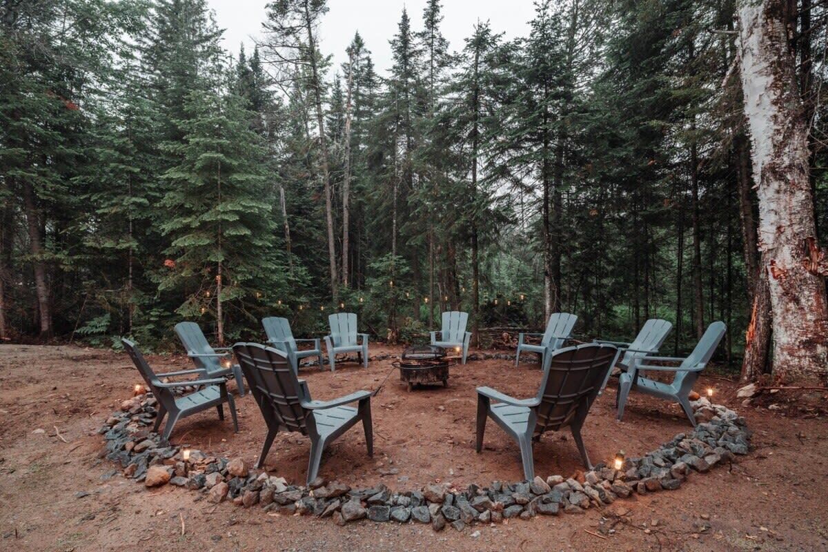 A circular seating area with chairs and a fire pit surrounded by rocks, set in a forested area.
