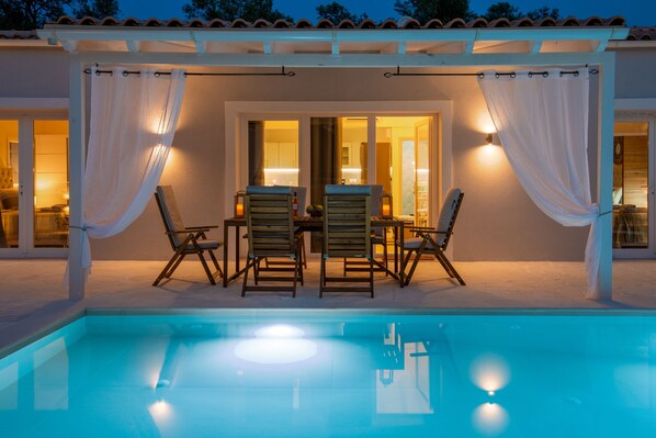 An outdoor pool area with a covered seating area and a view of the pool.