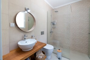 A bathroom with a round mirror, a white sink, a toilet, and a glass-enclosed shower.