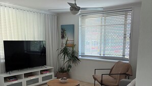 A living room with a flat-screen TV, a sofa, a coffee table, a potted plant, and a window with blinds. - Centrally Located Coastal Getaway – Walk to Beaches, Cafes & More (Miami)