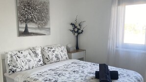 A bedroom with a bed, a nightstand, a vase with flowers, and a painting on the wall. - Centrally Located Coastal Getaway – Walk to Beaches, Cafes & More (Miami)