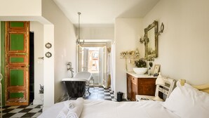 A hotel room with a checkered floor, a bed with white linens, a vintage bathtub, a wooden dresser, and a mirror on the wall. - Mediterranean Retreat 2-BR Apt w Rooftop (Tel Aviv)