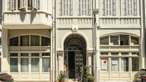 A building with a double door entrance, multiple windows with shutters, and potted plants in front. - Mediterranean Retreat 2-BR Apt w Rooftop (Tel Aviv)