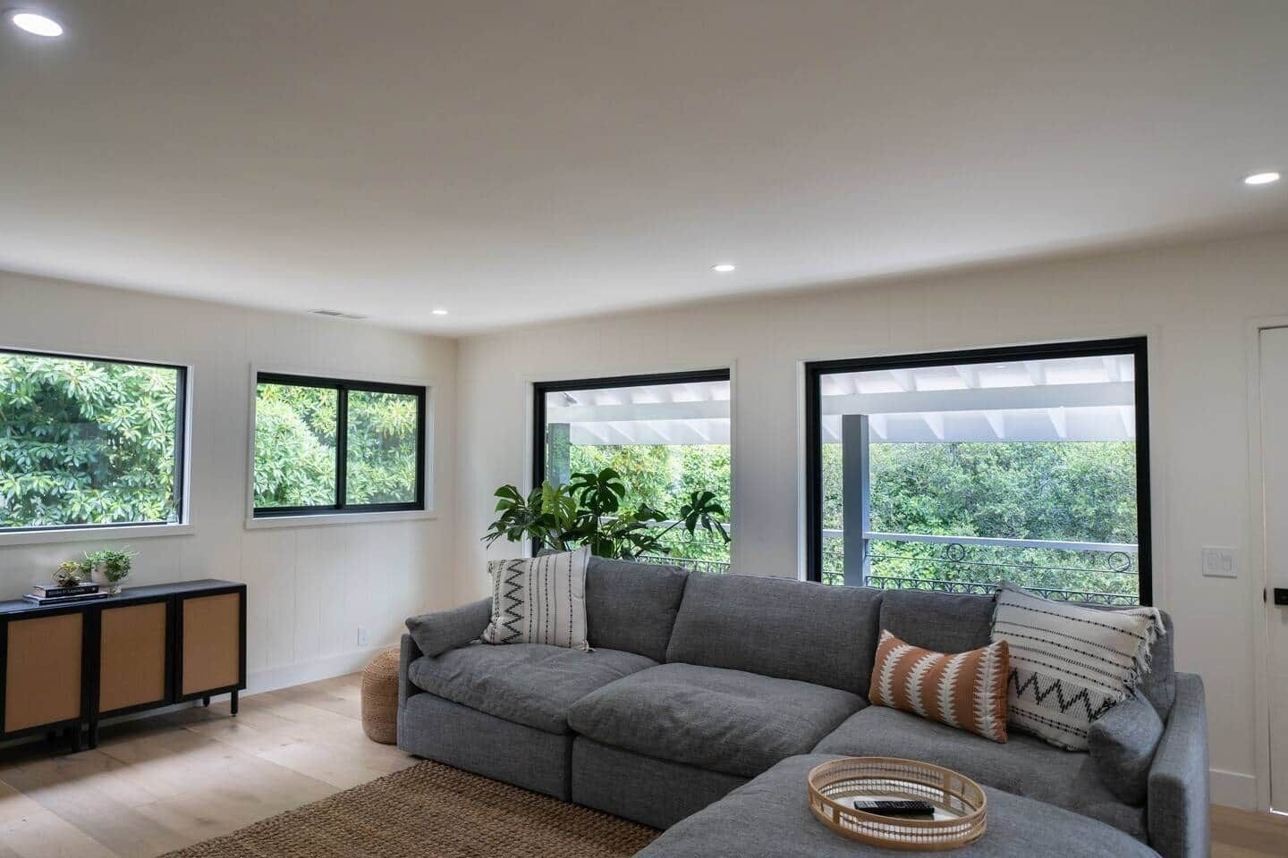 A modern living room with a grey sectional sofa, a small side table, and a large window with a view of greenery.