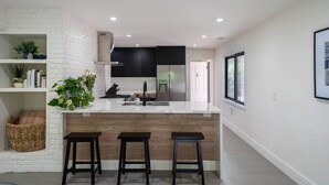Een moderne keuken met een witte bakstenen accentmuur, een centraal eiland met krukken en een zwarte achterwand.