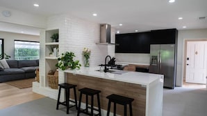Een moderne keuken met een witte bakstenen spatwand, zwarte barkrukken en een roestvrijstalen koelkast.