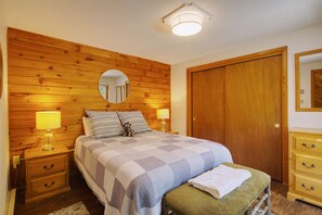 Una camera da letto con una testiera in legno, un letto con copripiumino a quadretti, due lampade sui comodini, un comodino, una cassettiera in legno e uno specchio appeso al muro.