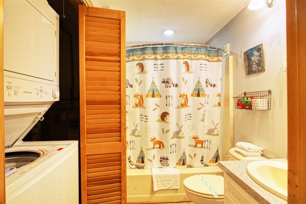 A bathroom with a shower curtain featuring animal prints, a toilet, a sink, and a washing machine.