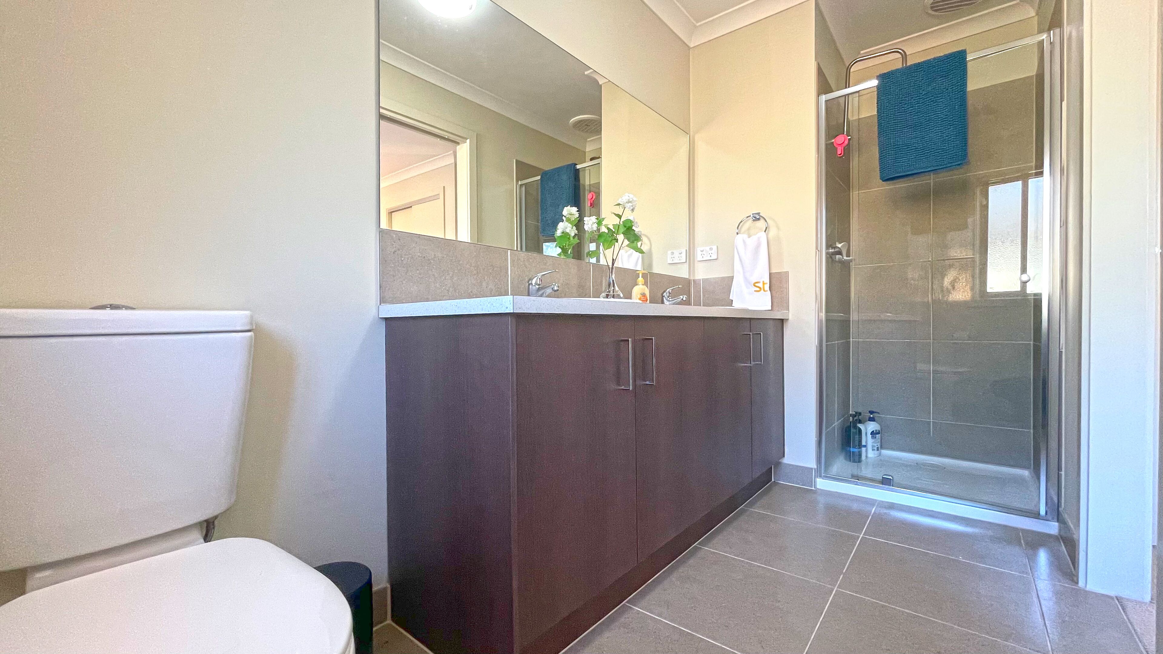 A modern bathroom with a toilet, dark wooden cabinets, a glass shower enclosure, and a mirror above the sink.