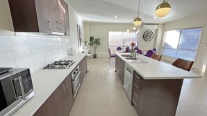 Une cuisine moderne dotée d’un îlot central, d’appareils électroménagers en acier inoxydable et de luminaires suspendus.