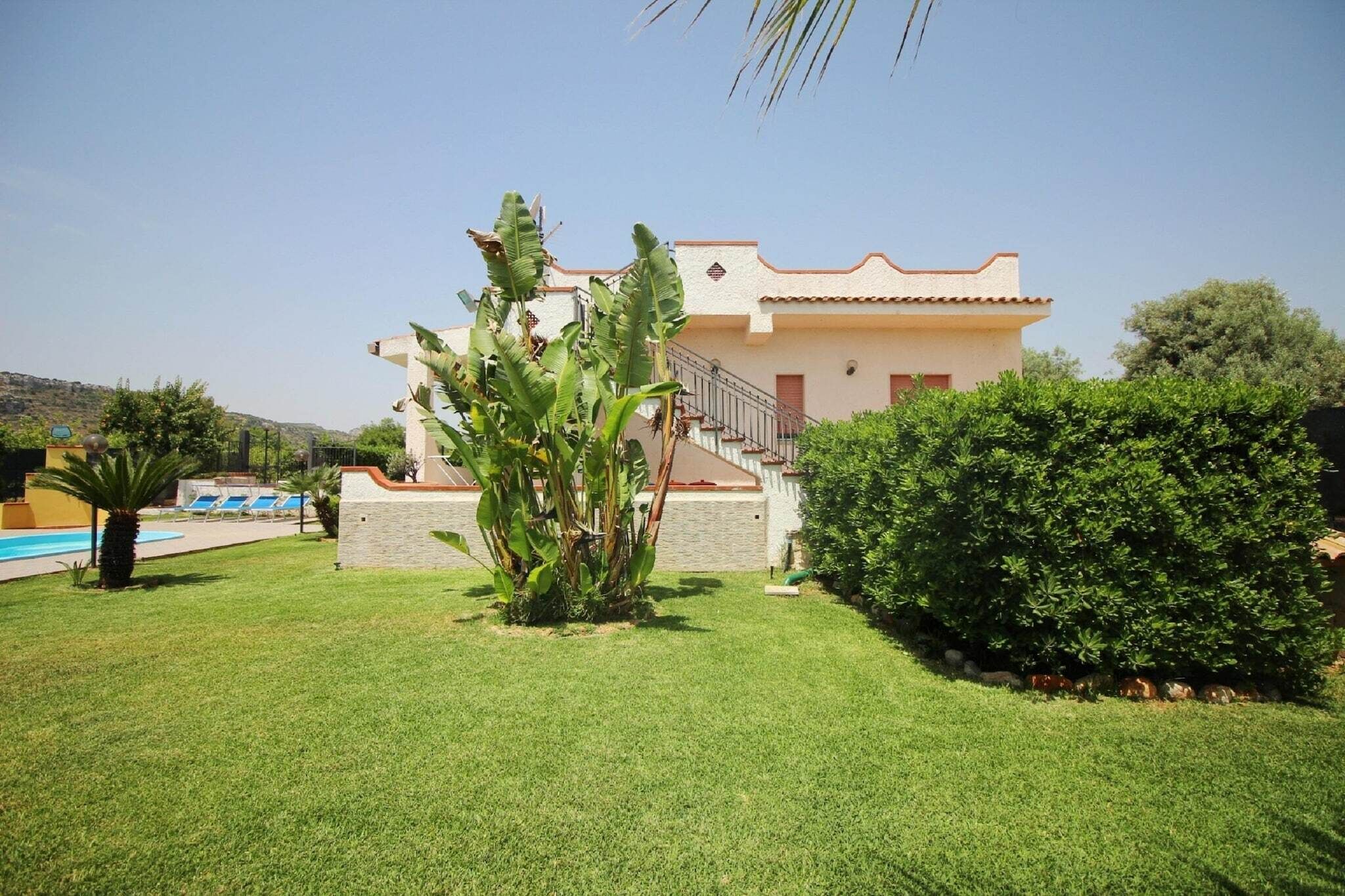 A two-story house with a pool, surrounded by well-maintained lawns and tropical plants.