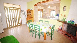 A dining area with a table set for four, surrounded by green chairs, a brick fireplace, and a kitchen area with a counter and cabinets.