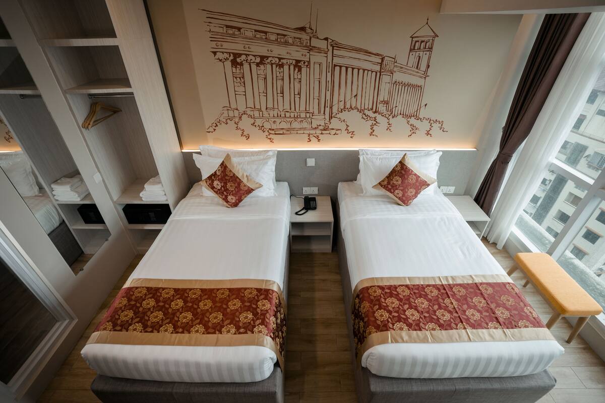 A hotel room with two beds, a nightstand, a small table, and a view of the city.
