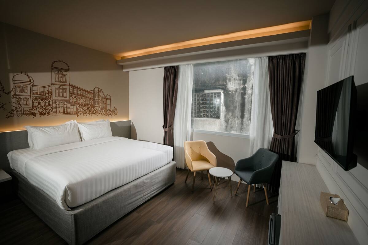 A modern hotel room with a large bed, a desk, a chair, a TV, and a window with curtains.