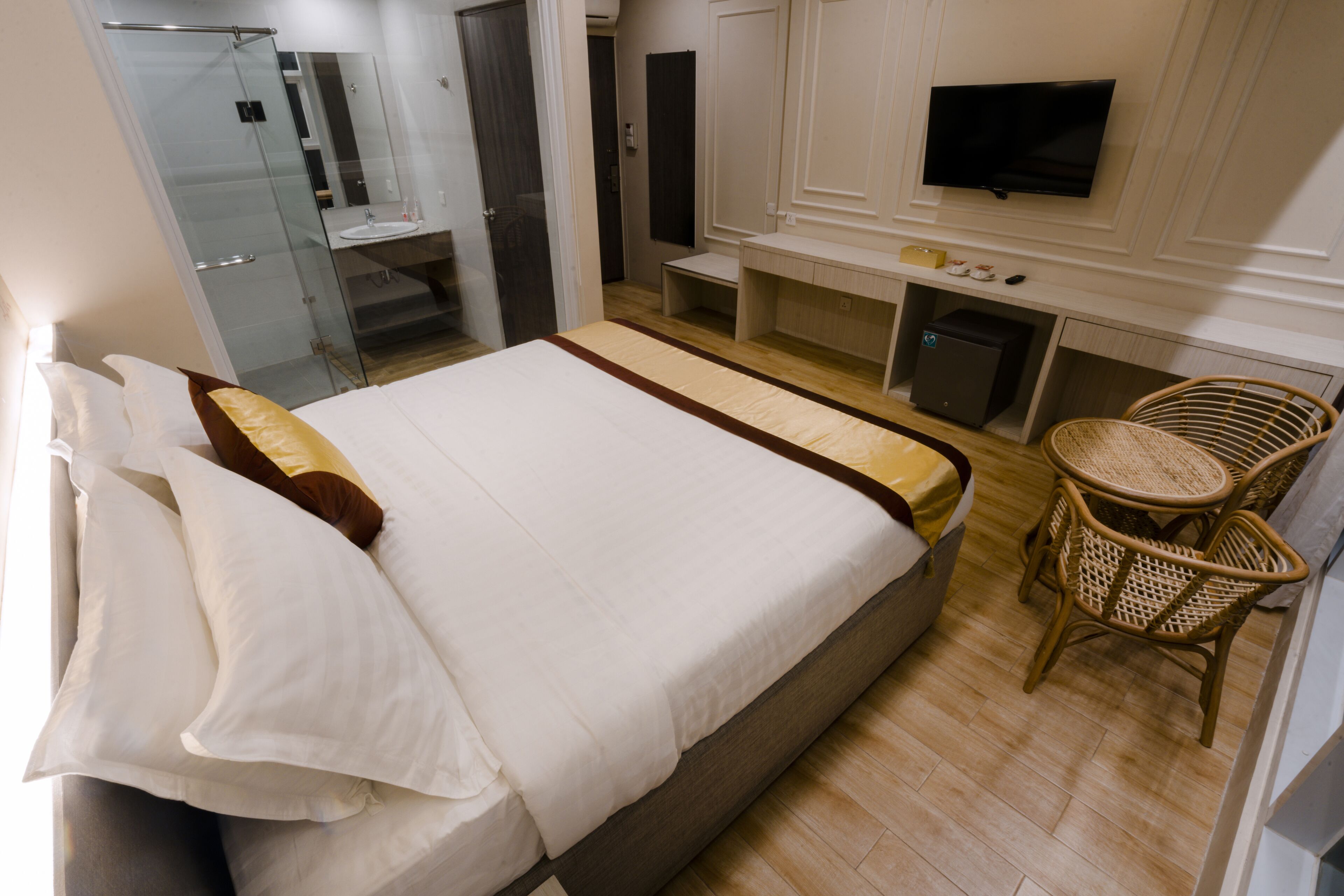 A hotel room with a large bed, a television, a small desk, and a wicker chair.