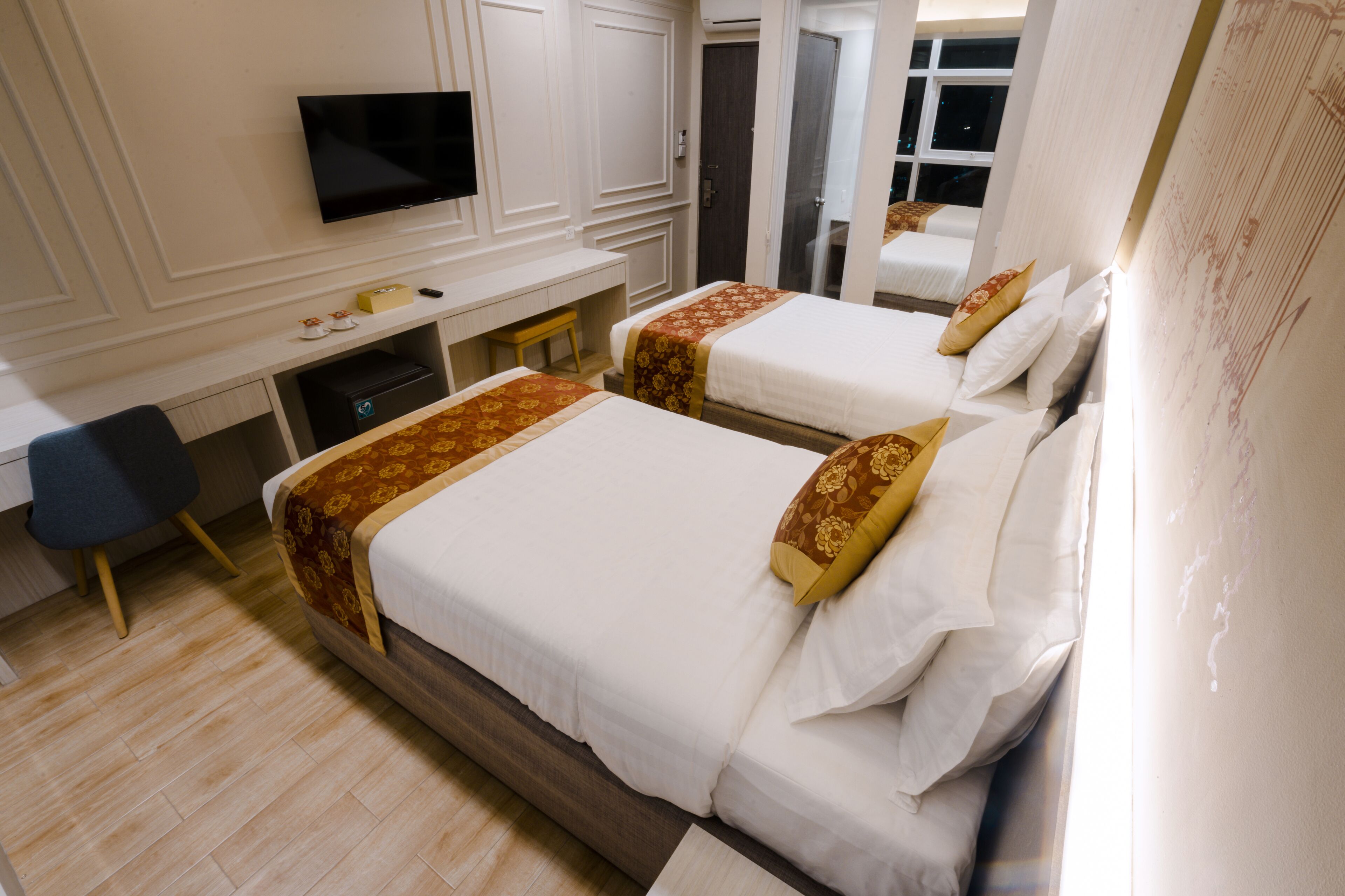 A hotel room with two beds, a desk, a chair, and a TV.