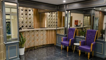 Un área de recepción con un revestimiento de pared de madera con diseño, una mesa de recepción y sillas moradas.