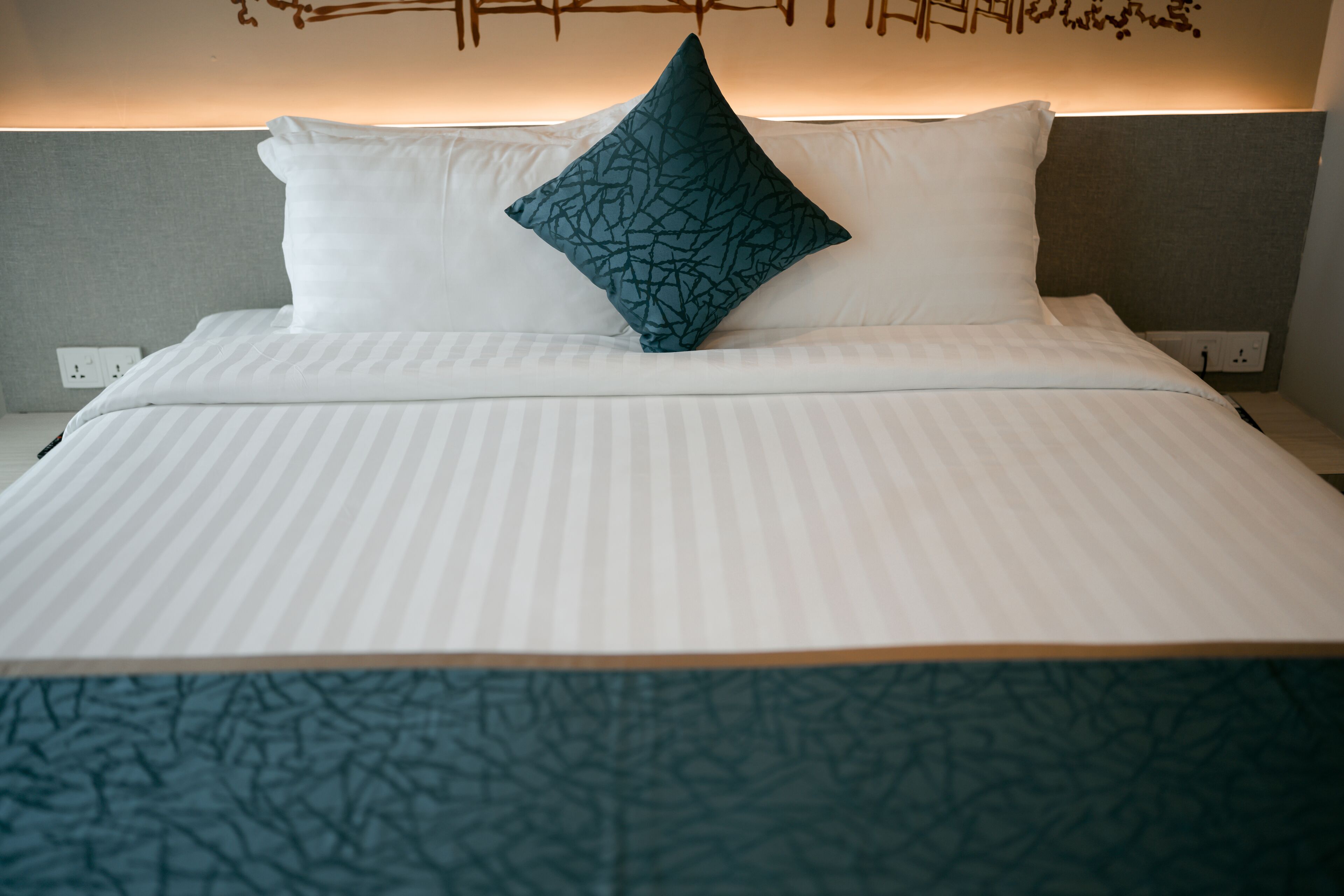 A neatly made bed with white bedding and a teal patterned pillow.