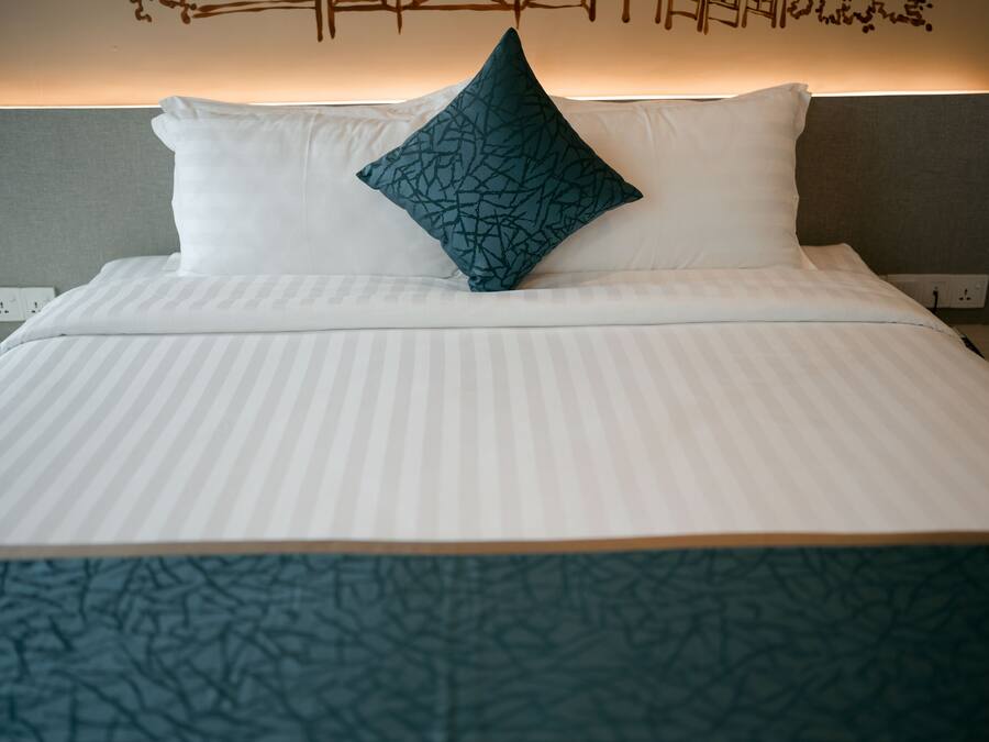 Una cama bien hecha con ropa blanca y una almohada de diseño azul turquesa.