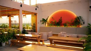 A modern indoor space with wooden tables and benches, a seating area with sofas, and a wall with a large illuminated orange circle.