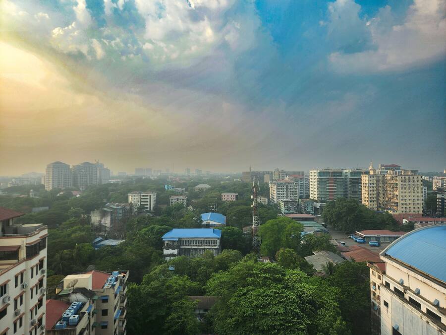 A cityscape with various buildings, including residential and commercial structures, under a cloudy sky.