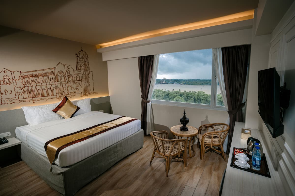 A hotel room with a bed, a small table with chairs, a TV, and a view of a body of water.