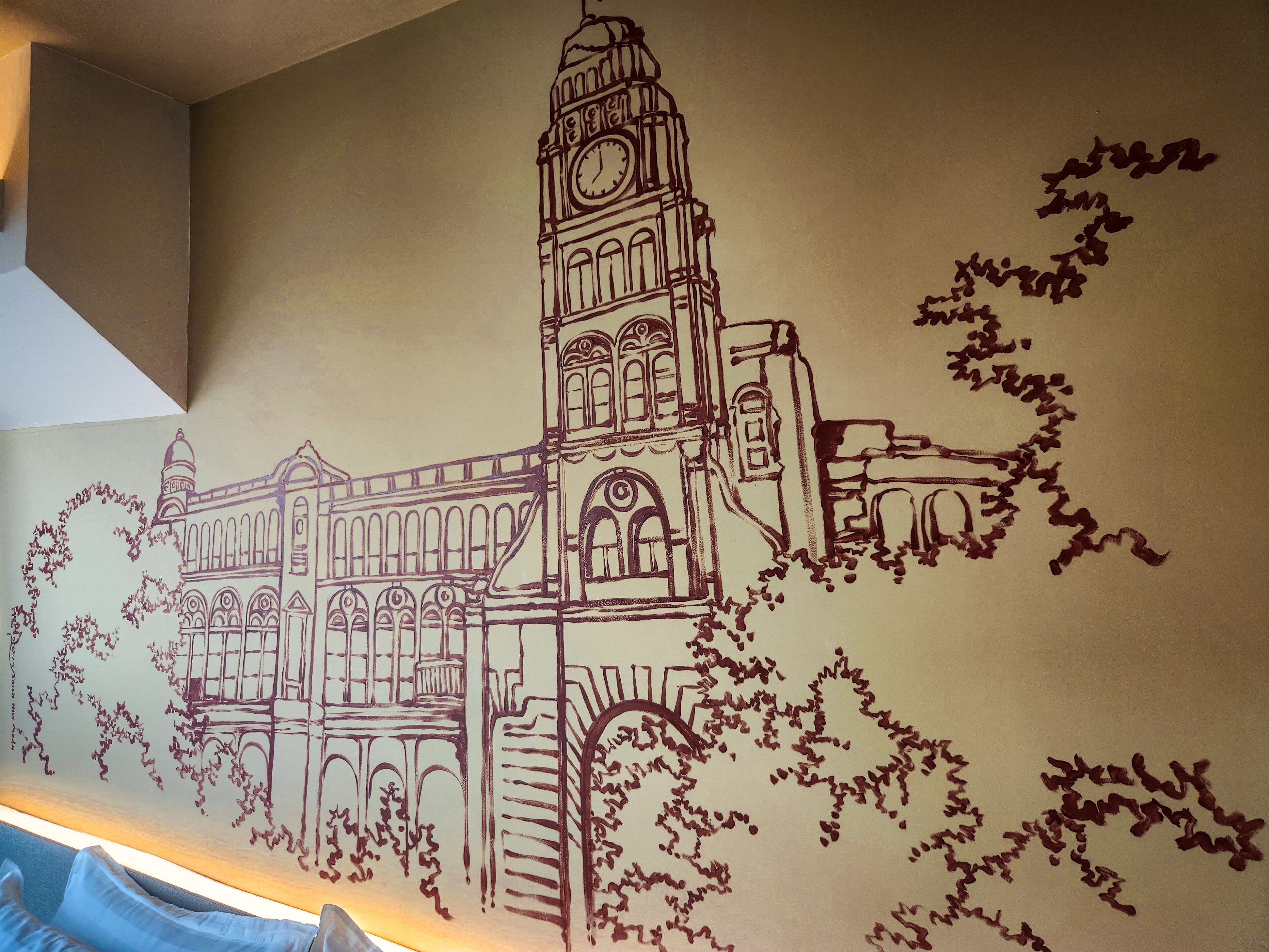 A wall mural of a historic building with a clock tower, arched windows, and foliage.
