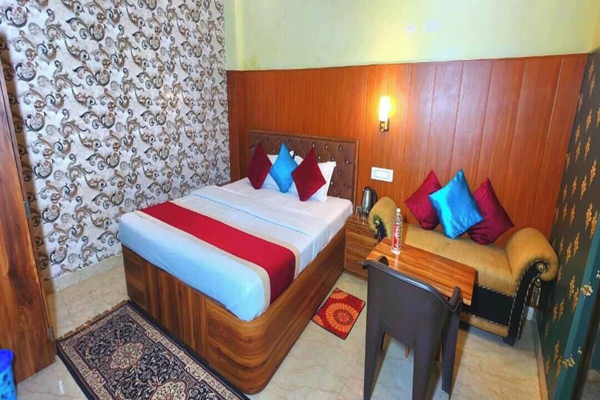 A hotel room with a wooden headboard, a bed with multiple pillows, a small desk with a chair, and a patterned rug.