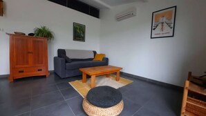 A living room with a sofa, a wooden cabinet, a coffee table, a rug, and a wall-mounted air conditioner. - Country house with garden ★ free pool and jacuzzi ★ Cévennes (Cros)