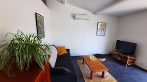 Ein Wohnzimmer mit einer Couch, einem Couchtisch, einem Fernseher und einer Topfpflanze.