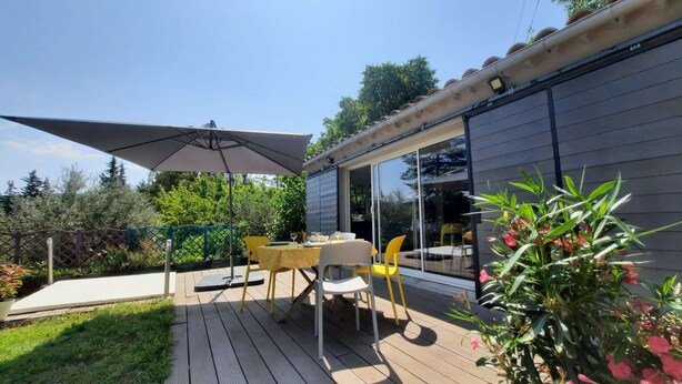 An outdoor patio with a table and chairs, a large umbrella, and a sliding glass door leading to a covered area. - Country house with garden ★ free pool and jacuzzi ★ Cévennes (Cros)