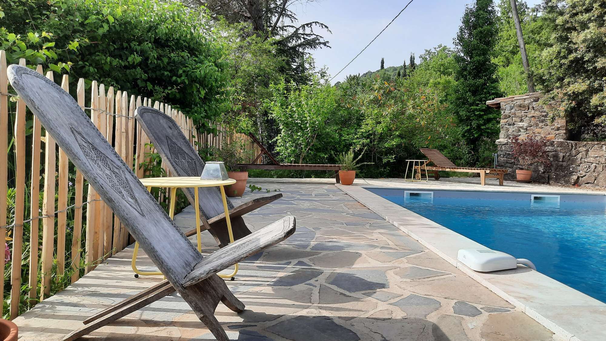 A pool area with a stone patio, a wooden fence, and a lounge chair.