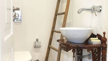 Een badkamer met een wit toilet, een houten trapje, een witte wasbak op een houten standaard en een spiegel aan de muur.