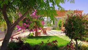 Un patio jardín con pared de piedra, mobiliario de madera y plantas en flor.