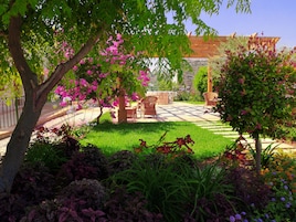 Un patio jardín con pared de piedra, mobiliario de madera y plantas en flor.