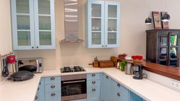 Una cocina con gabinetes azul claro, una campana extractora de acero inoxidable, un horno empotrado, un microondas y una cafetera.